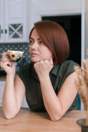 Portrait of a woman with bob haircut and red natural hair in everyday life at home with a cup of tea...