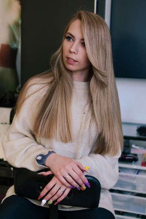 Blonde girl with beautiful long hair on a dark background indoorsの写真素材