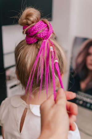 Pink colored braids on a girl blonde 5 years old close-up indoorsの写真素材