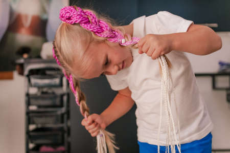 Front view of a girl with blond hair five years old with a hairstyle of pink braids indoorsの写真素材