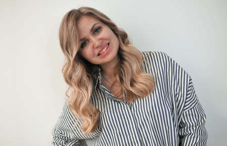 portrait of young blonde woman with gorgeous curly hair and blue eyes indoors, front viewの写真素材