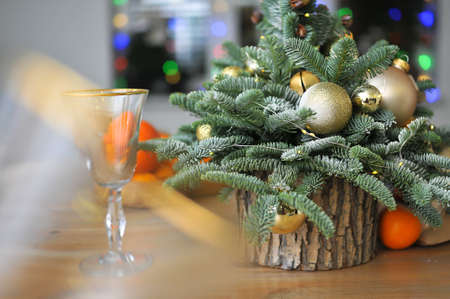 Christmas composition - a small natural Christmas tree decorated with golden toys with tangerines and glasses on the tableの写真素材