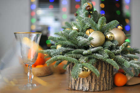 Christmas composition - a small natural Christmas tree decorated with golden toys with tangerines and glasses on the tableの写真素材