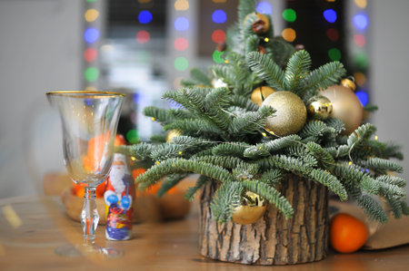 Christmas composition - a small natural Christmas tree decorated with golden toys with tangerines and glasses on the tableの写真素材