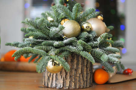 Christmas composition - a small natural Christmas tree decorated with golden toys with tangerines on the tableの写真素材