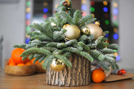 Christmas composition - a small natural Christmas tree decorated with golden toys with tangerines on the tableの写真素材
