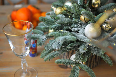 Christmas composition - a small natural Christmas tree decorated with golden toys with tangerines and glasses on the tableの写真素材