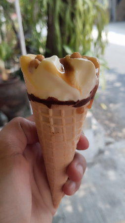 ice cream in a waffle cone with chocolate and caramel in hand. Selective focus, hand held chocolate ice cream with blurred backgroundの写真素材