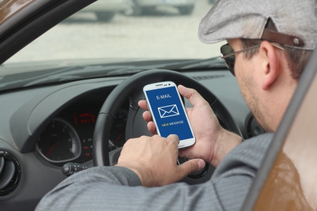 Happy male driver smiling while sitting in a car with open front window and checking email on mobile...