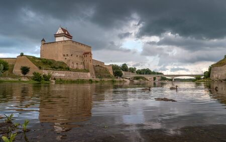 Narva Castle in Estonia on the background of a stormy sky. Ducks swimming on the background of bridge.の写真素材