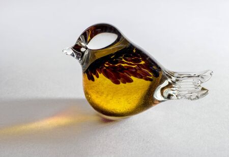 Glass statuette of a bird. Yellow glass soldered with additional decorative elements. A figurine on a white background, the light is reflected on the background. Bird as a great bird.の写真素材