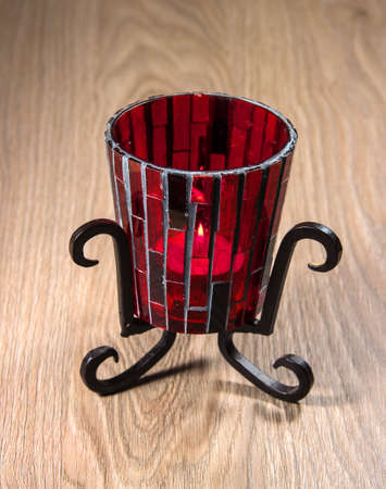 Candlestick from red glass on a metal stand. Candlestick stands on a wooden table.の写真素材