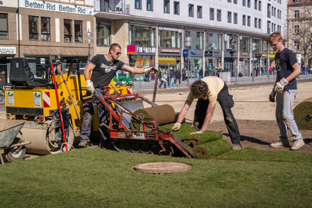 Munich, Germany April 13, 2013: Mechanized laying a new lawn. For laying the lawn using a special truck crawler. One worker controls the trolley and the other leveled lawn.のeditorial素材