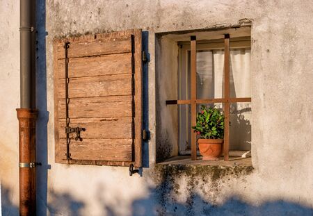 Old window with open shutters with flowers on the window sill on the stone wall. Italian Village. To the left of the window is the downspout.の写真素材