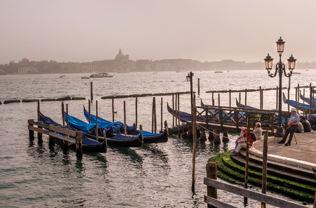 Venice, Italy - October 13, 2017: Evening view of the Grande Canal. Tourists admire the view. In the foreground are moored gondolas. The steps of the parapet are overgrown with green algae.のeditorial素材