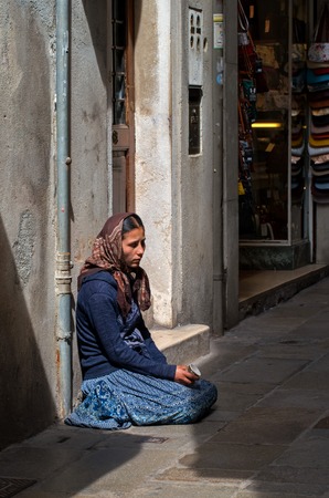Venice, Italy - May 07, 2018: A homeless female beggar is begging on the street in Venice, Italy. A beggar woman holds a cardboard Cup in her hand for almsのeditorial素材