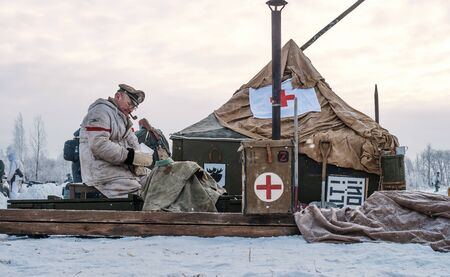 Krasnoye Selo, St. Petersburg, Russia - January 19, 2019: Military historical reconstruction - the battle for Leningrad. Military field hospital of the German army. Medical orderly smoking a pipe.のeditorial素材