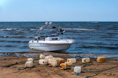 The motorboat moored to the sandy shore. Floats made of plastic cans. The beach of the Gulf of Finlandの写真素材