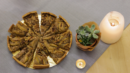 Kraft pie with nuts and fruits on the festive wooden table with candles and home plant cactus on a gray tableclothの写真素材