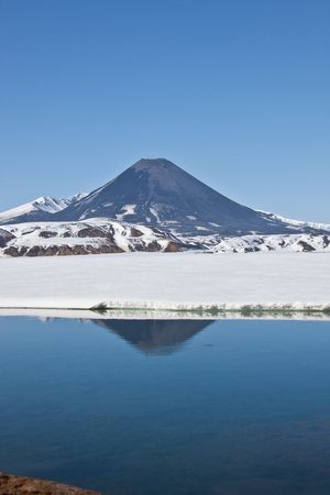 Look at Karymsky volcano from the hot springs and geyser Karymsky lake in spring in Kamchatka, Russia, snow, may, reflectionの写真素材