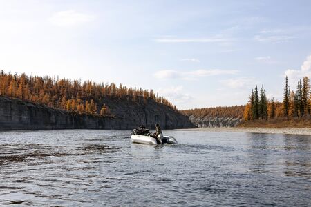 Autumn rafting on a boat with fishing on the Siberian river.  A fisherman on an inflatable boat with...