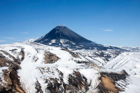 View of the correct cone of the Karymsky volcano in the spring after a snowfall. Geothermal activity...