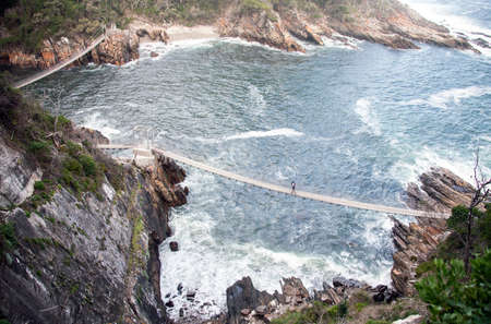 Suspended pedestrian bridges over the cliffs and bays in the Park Tsitsikama. Silhouettes of...