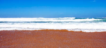 Ocean surf on a sandy beach on a Sunny day. Foam, spray and waves of sea water at the edge of the...