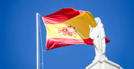 Coat of arms on the flag of Spain in the blue sky of Barcelona. National flag of Spain on a flagpole in a clear Sunny summer sky.の写真素材