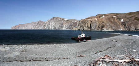 Landscape of the northern sea coast with tugboat and boat on the shingle shore. The coastline of the...