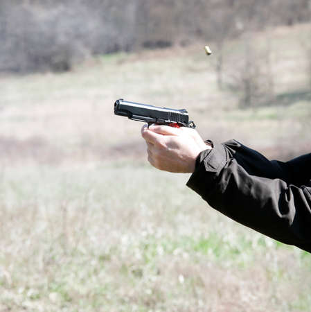 Black pistol in the hands of the shooter and a flying cartridge case at the time of the shot. A...