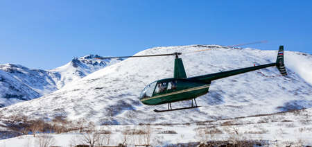 Green helicopter with masked passengers flies over a mountainous area. Small helicopter in flight...
