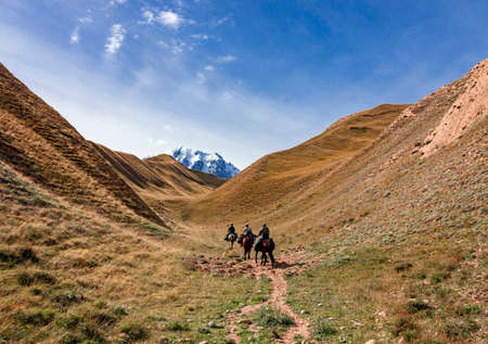 Riders with weapons and cargo climb the mountains on horseback. Three men on loaded horses climb up a mountain ravine.の写真素材