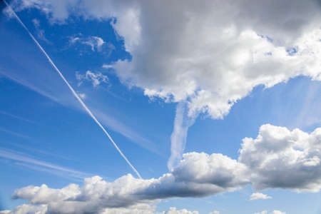 Contrails from an airplane among clouds on blue sky background. White clouds and traces of flying...