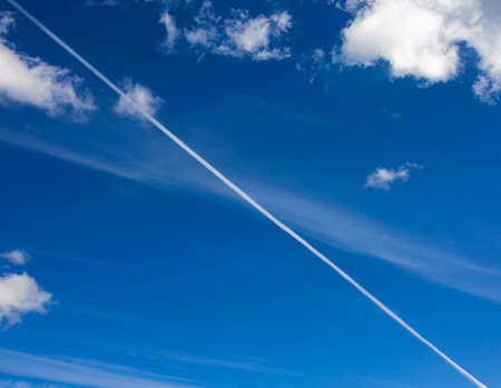 Diagonal of the white contrail from the plane divides the azure sky. View of  cloudy landscape on  blue sky in early autumn.の写真素材