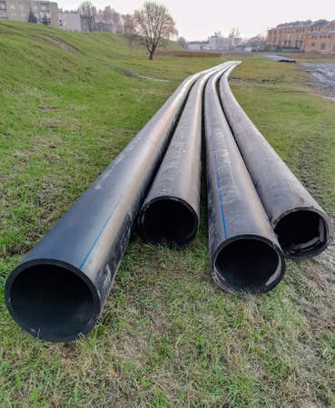 Large-diameter plastic pipes lie on the ground surface before installation. Construction of a new...