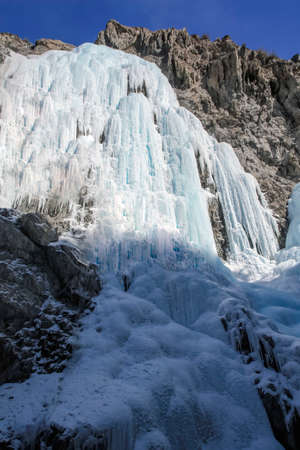 Icy streams of water frozen on the rocks against the blue sky. An ice waterfall in the mountains in clear sunny weather.の写真素材