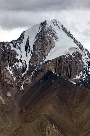 Beautiful high mountain with rocks, snowfields, glaciers and rocky scree. Mountain peak in autumn cloudy weather in an Asian mountain country.の写真素材