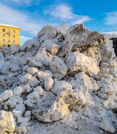 Mountain of packed snow from the streets and squares of Saint-Petersburg against the sky. Blocks and chunks of ice and snow are stored in the park against the background of the blue sky.の写真素材
