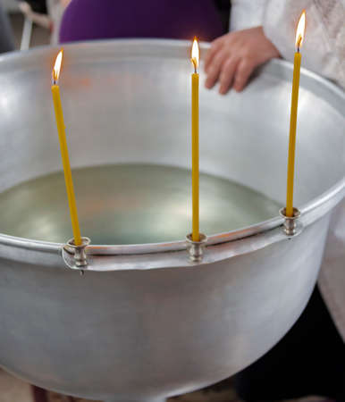Three burning candles on the edge of the silver font before the Orthodox rite of baptism of a child. Wax candles with flames before the Christian baptism ritual in the church.の写真素材