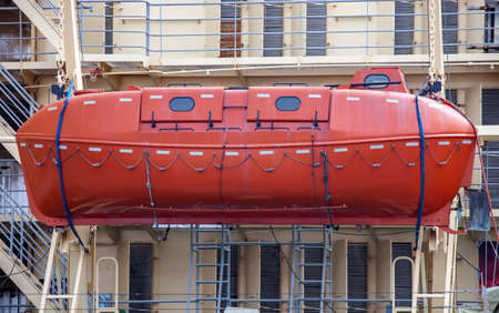 An orange closed-type Arctic lifeboat on board an icebreaker. Rescue weltbot on the background of the superstructure and the rails of marine vessel.の写真素材