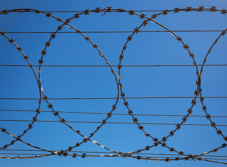 Flat security barrier made of reinforced barbed tape on the fence. Barbed wire fence against clear...