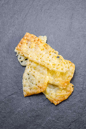 Top view of tasty homemade food, showing golden cheese chips cracker made of gouda cheese slices and salt placed on a dark stone granite underground. Use for food blog or DIY fast food for a party.の写真素材