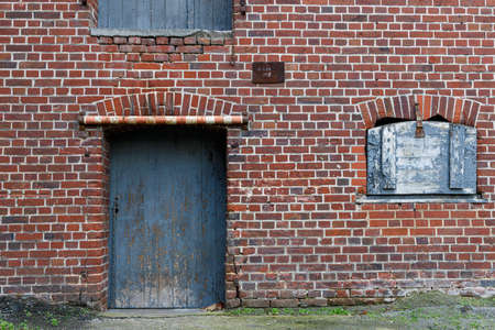 Texture view, a red and weathered brick wall with a blue old door and a small window with a closed...