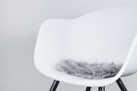 Side view of a modern white plastic chair with a seat cushion made of gray artificial long fur, use as design background for interior scene.の写真素材