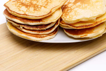 Two stacks of homemade pancakes on a bamboo cutting board on white uniform background, perspective...