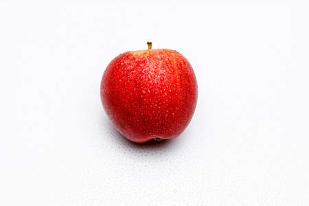 One red and fresh apple on white uniform background with small water sprinkles and soft shadows, use...