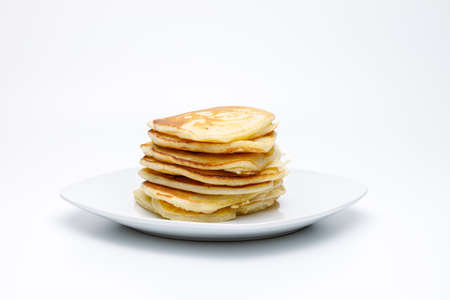 Side view of a pile or stack of pancakes on a white plate on a white and uniform background, typical American homemade food for breakfastの写真素材