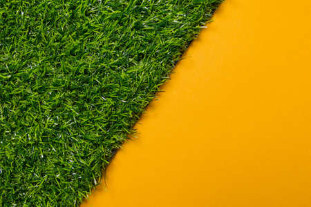 Top view of artificial grass on a yellow uniform background, the image is cut diagonal by the plastic gras, use as template or backgroundの写真素材