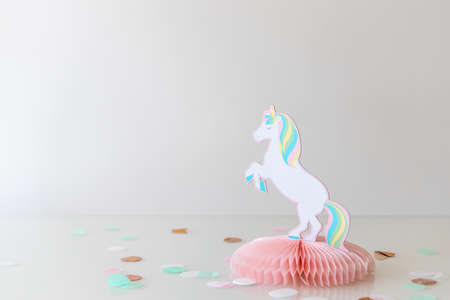 Girls party decoration with a unicorn made of paper and confetti dots on a glas table, white and...